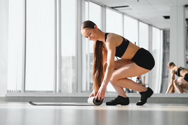 Temps pour le concept de bien-être de la séance de remise en forme de méditation Fille portant un pantalon de sport gris roulant un tapis de fitness avant après les cours dans un club de studio de yoga ou à la maison sur un plancher en bois Mains et jambes en gros plan