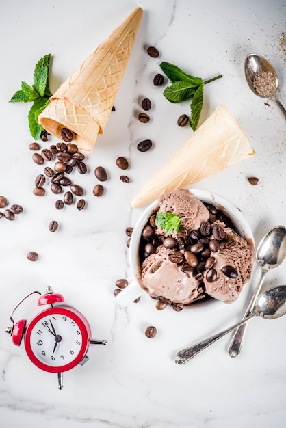 Temps pour le concept de café, avec un réveil pendant des heures dans le cadre. Glace au café faite maison, servie avec des grains de café et des feuilles de menthe, avec des cornets de crème glacée, des cuillères. Fond de marbre blanc, ci-dessus