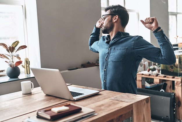 temps de repos. beau jeune homme s'étirant tout en travaillant au bureau