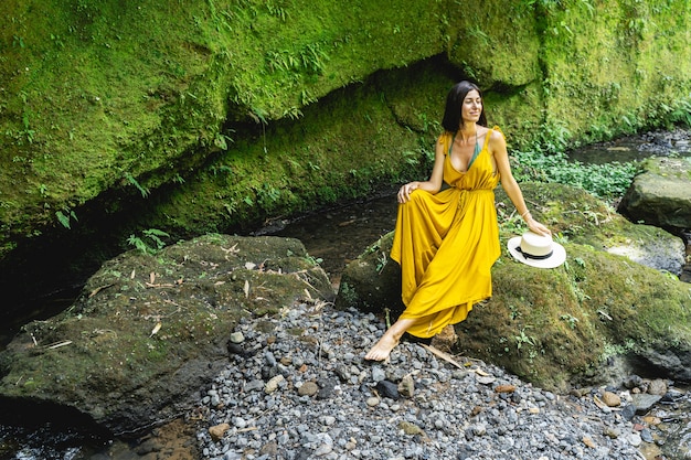 Le temps de se détendre. Jolie jeune femme exprimant sa positivité tout en écoutant de l'eau courante près du ruisseau