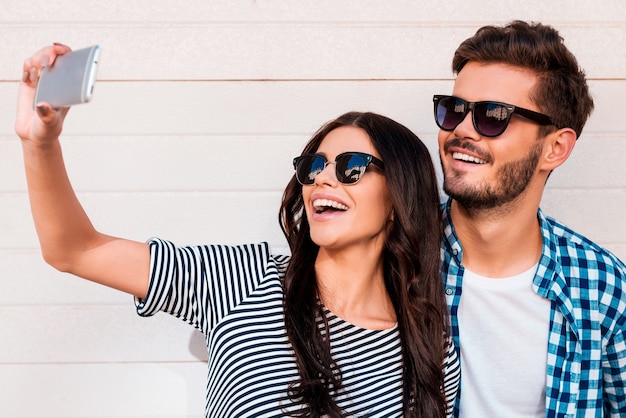 Temps de selfie. Beau jeune couple d'amoureux faisant selfie sur téléphone intelligent tout en se tenant à l'extérieur