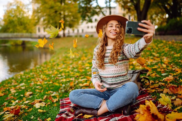 Temps de selfie Belle femme prend selfie sur smartphone en chapeau sur prairie dans le parc d'automne sur plaid