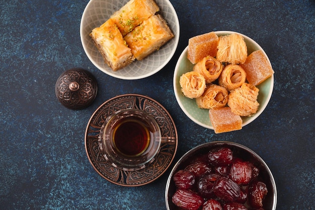 Temps de thé chaud arabe frais avec des bonbons baklava dattes lokum d'en haut de Ramadan collation avec des délices turcs et des pâtisseries arabes sur fond rustique bleu vue supérieure