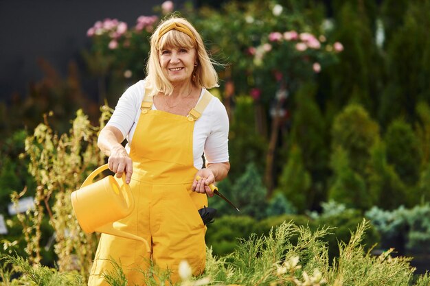 Tenant un arrosoir jaune Une femme âgée est dans le jardin pendant la journée Conception des plantes et des saisons