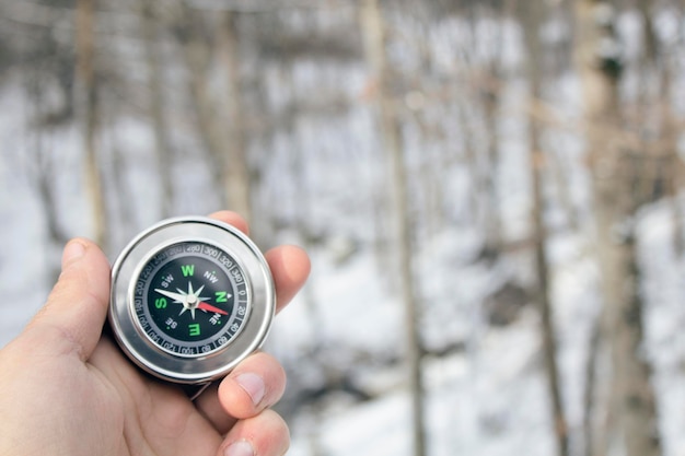 Tenant une boussole sur le fond de la forêt d'hiver