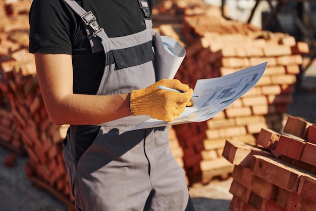 Tenant le plan entre les mains Un ouvrier du bâtiment en uniforme et équipement de sécurité a un travail sur la construction