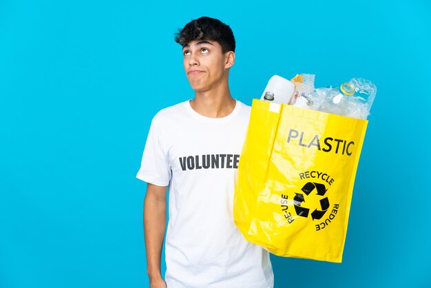 Tenant un sac plein de bouteilles en plastique à recycler sur bleu et levant