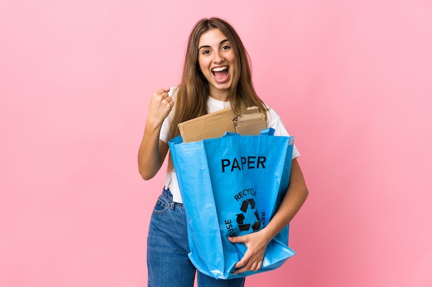 Tenant un sac de recyclage plein de papier à recycler sur rose isolé célébrant une victoire