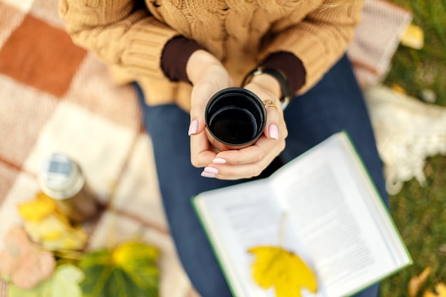 Tenant une tasse de thé chaud dans un parc en automne