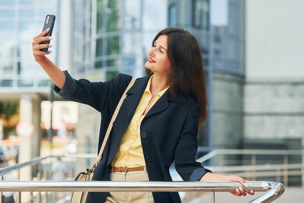 Tenant le téléphone à la main Femme en tenue de soirée debout à l'extérieur de la ville pendant la journée