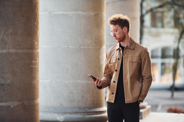 Tenant le téléphone à la main Jeune homme élégant dans des vêtements chics formels à l'extérieur de la ville