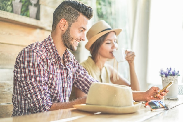 Tendance jeune couple buvant du café et utilisant un smartphone dans un café-bar