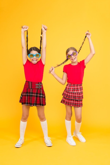 Tendance de la mode estivale. Amis à la mode pour enfants posant dans des lunettes de soleil sur fond jaune. Plaisirs de l'été. Accessoire d'été. Les tenues similaires des sœurs mignonnes des filles portent des lunettes de soleil colorées pour la saison estivale.