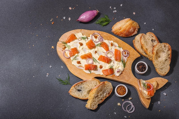 La tendance de la nourriture au beurre sur la table surmontée de salmons, d'échalote et de verts frais Appétisant pour une fête, des morceaux de baguette durs, clair, ombre sombre, fond de béton en pierre noire, vue supérieure plate.