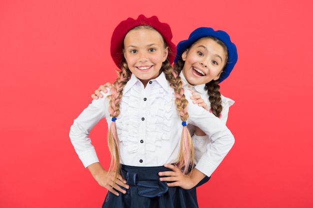 Les tendances de la mode dont toutes les filles ont besoin pour la rentrée scolaire. Des écoliers heureux avec un look fashion sur fond rose. Petites filles aux tresses de cheveux longs souriant dans des bérets de mode. Mode pour les petits étudiants.