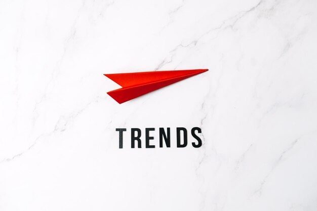 Les tendances mondiales mondiales sont les principales nouvelles tendances prévoyant les tendances des mots et l'avion en papier rouge sur fond rouge