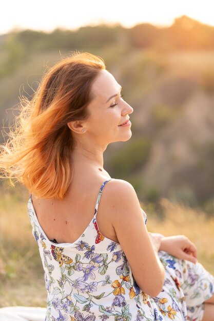 Tendre belle fille rousse profite du coucher de soleil dans un champ avec une colline