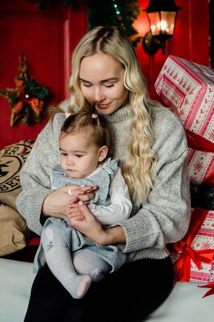 Photo tendre jolie maman embrasse sa fille sur fond de noël. vacances en famille, cadeaux, noël, concept de noël