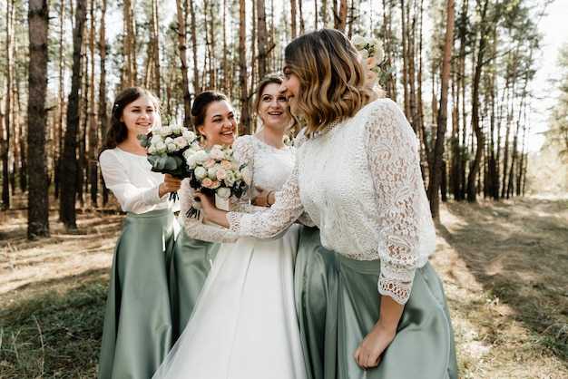 Tendre mariée avec des demoiselles d'honneur souriantes vêtues de longues robes élégantes, demoiselles d'honneur avec une mariée heureuse le jour du mariage. les bouquets de mariage sont tenus par des copines, le jour du mariage,