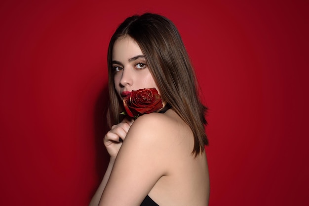 Tendresse et beauté jeune femme tenant une fille de beauté rose avec une rose rouge près du visage tourné en studio romain