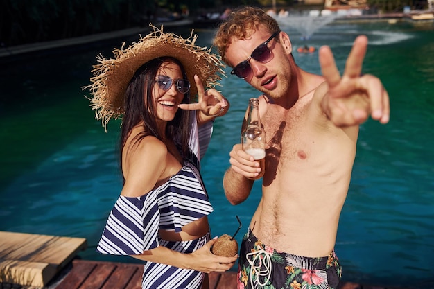 Tenir des boissons dans les mains Joyeux couple ou amis ensemble dans la piscine en vacances