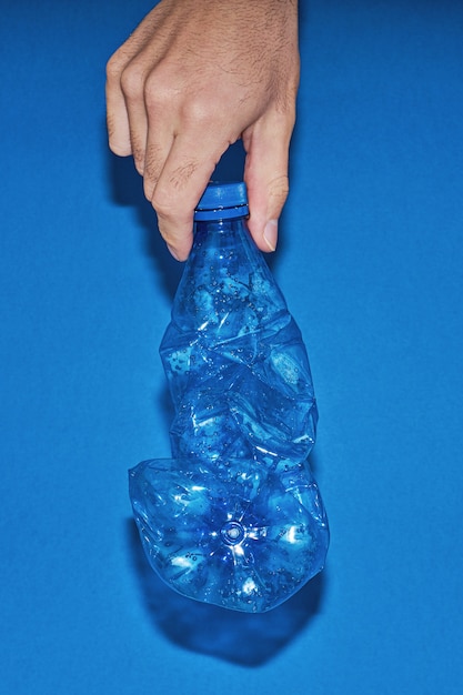 Tenir la main bouteille en plastique pressé sur bleu
