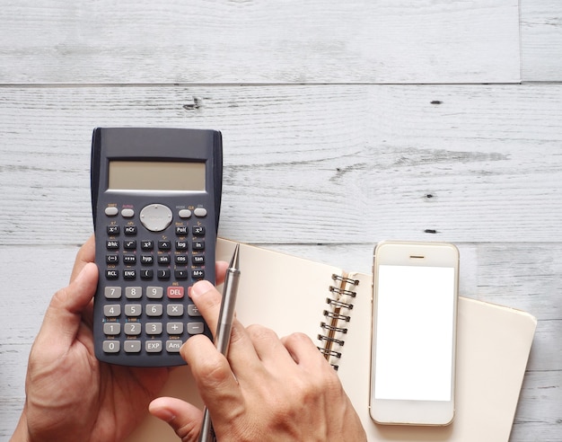 Tenir la main à l'écran blanc du téléphone portable à l'aide d'une calculatrice avec un stylo cactus sur le concept d'entreprise de la vue de dessus de table