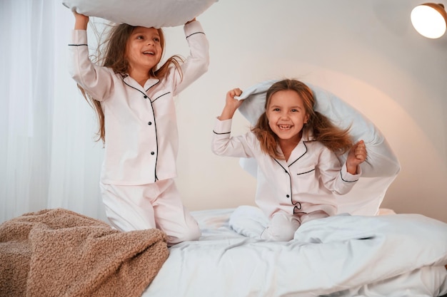 Photo tenir des oreillers et jouer deux petites filles s'amusent ensemble dans la chambre domestique