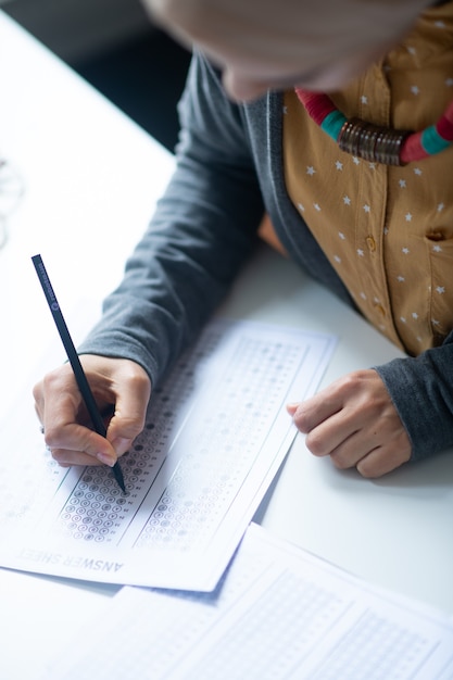 Tenir un stylo. Jeune enseignant portant un joli collier tenant un stylo tout en vérifiant les tests