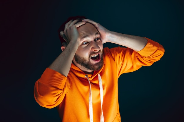 Tenir la tête. Portrait d'un homme caucasien fou effrayé et choqué isolé sur fond sombre. Copyspace pour l'annonce. Expression faciale lumineuse, concept d'émotions humaines. Regarder l'horreur à la télévision, au cinéma.