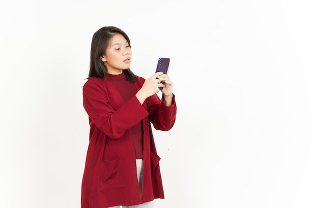 Tenir et utiliser le smartphone de la belle femme asiatique portant une chemise rouge isolée sur fond blanc