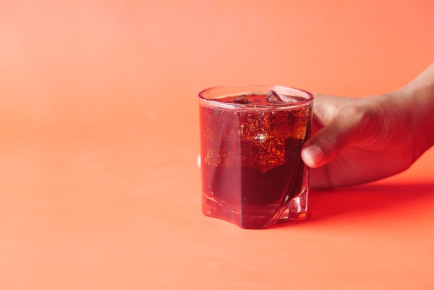 Tenir un verre de boisson gazeuse sur fond rouge