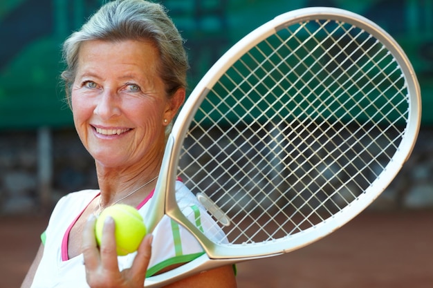 Le tennis est son jeu Senior woman smiling tout en tenant une raquette de tennis et une balle