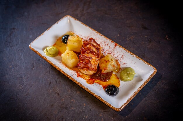 Tentacule de poulpe avec pommes de terre sur fond noir, sur une plaque blanche