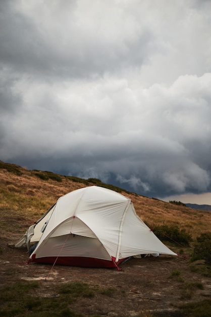 Tente blanche dans un pré avec vue sur la chaîne de montagnes avec des nuages de pluie devant la montagne des Carpates Ukraine Sentiers de marche et de randonnée dans la crête de Marmaros Camping dans les montagnes des Carpates en automne