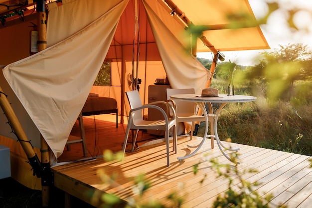 Tente de glamping ouverte confortable avec lumière à l'intérieur pendant le coucher du soleil Tente de camping de luxe pour les vacances d'été en plein air et les vacances Concept de style de vie