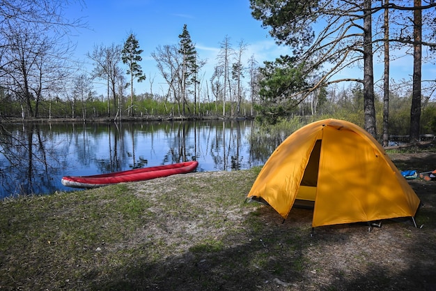 Une tente jaune sur la rive d'une rivière forestière