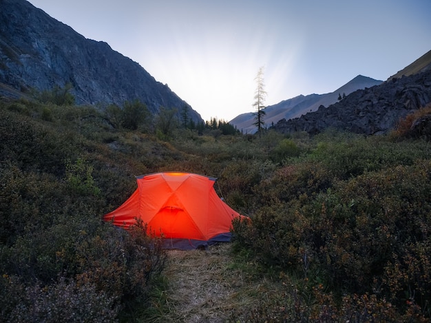 Tente orange Gowing au crépuscule dans les montagnes. Camping confortable dans les montagnes fraîches d'automne.