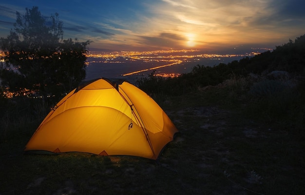 Photo tente touristique orange sur fond de lumières de la ville au coucher du soleil