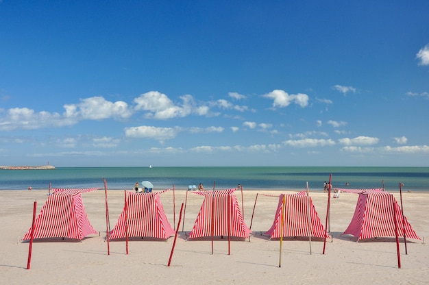 Tentes rouges et blanches sur une plage presque déserte avec une mer calme Certaines personnes bronzent sur le sable