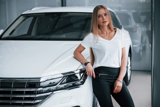 En tenue décontractée. Fille et voiture moderne dans le salon. Le jour à l'intérieur. Achat de véhicule neuf.