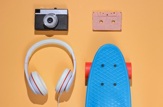 Photo tenue hipster. skateboard avec casque, cassette audio sur fond de couleur jaune. minimalisme de la mode créative. style rétro tendance des années 80. amusement d'été minimal. notion musicale. vue de dessus
