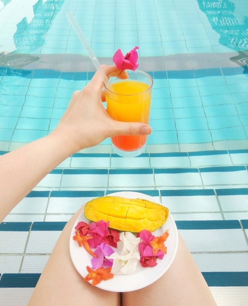 Tequila sunrise ou jus d'orange dans la main de la femme a servi des bougainvilliers de fleurs tropicales de mangue dans la piscine. Lifestyle vocation relax repos spa