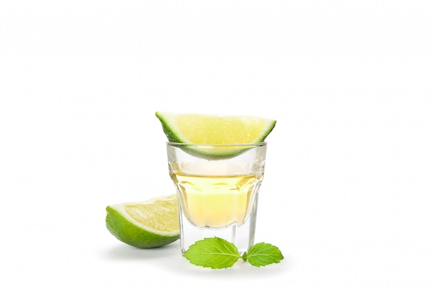 Tequila tourné avec des tranches de citron vert et de menthe isolé sur blanc