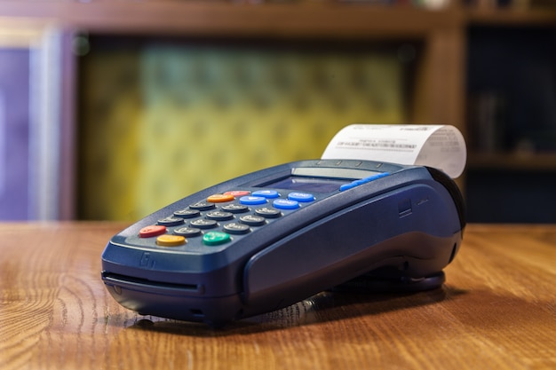 Photo terminal de banque avec un chèque imprimé et des boutons de couleur debout sur une table en bois. le concept de paiement des factures au restaurant et boutique, shopping par carte de crédit