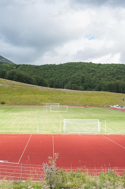 Photo un terrain de football vide par les montagnes contre un ciel nuageux