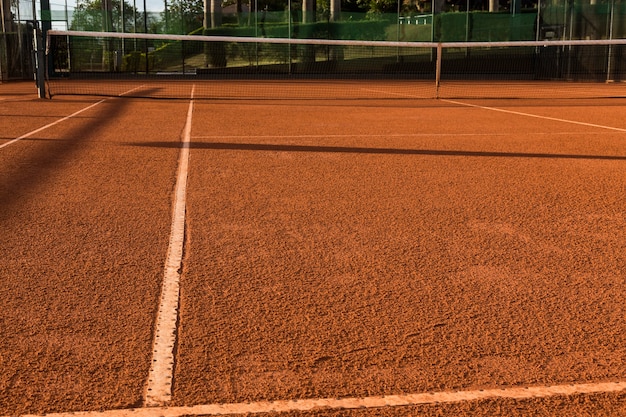 Terrain de tennis en terre battue, sous le coucher du soleil.