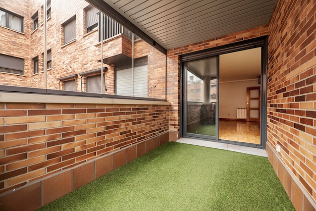 Terrasse fermée avec briques brunes en verre et en métal et sol en gazon artificiel vert dans des logements résidentiels urbains