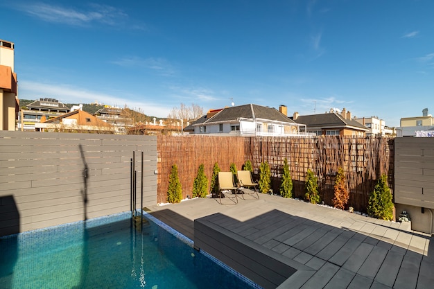 Terrasse privée sur le toit d'une maison avec transats de piscine et clôture en bois aux beaux jours en b...