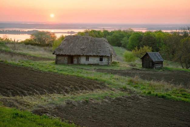 Terres agricoles près de la vieille maison en bois abandonnée en Ukraine. Paysage rural avec rivière au lever du soleil. Chemin vers la maison.